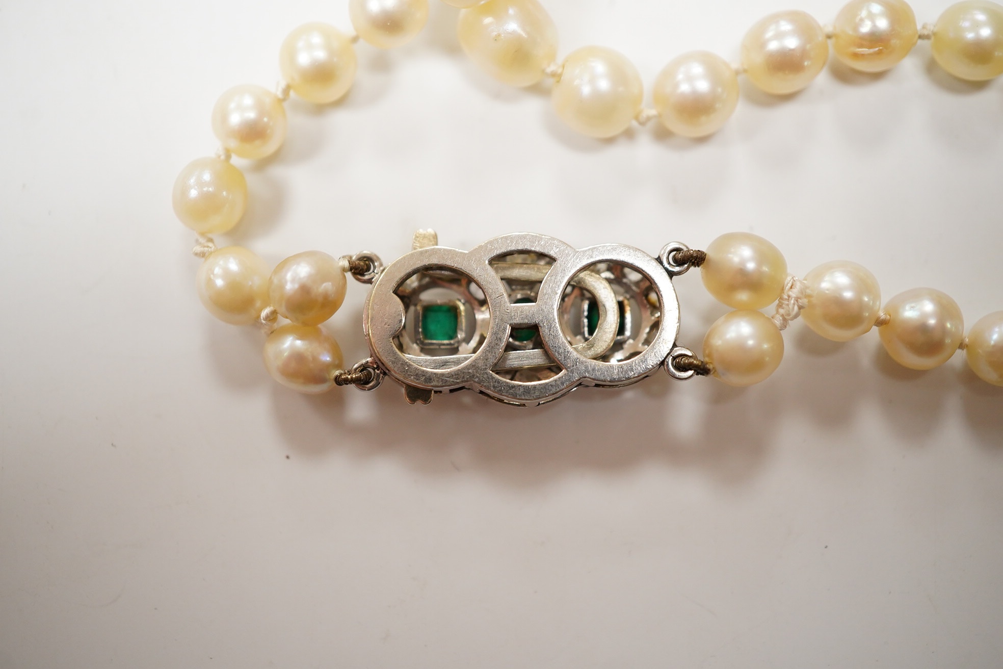 A single strand cultured pearl necklace, with and emerald and diamond cluster set white metal clasp, 76cm. Condition - fair.